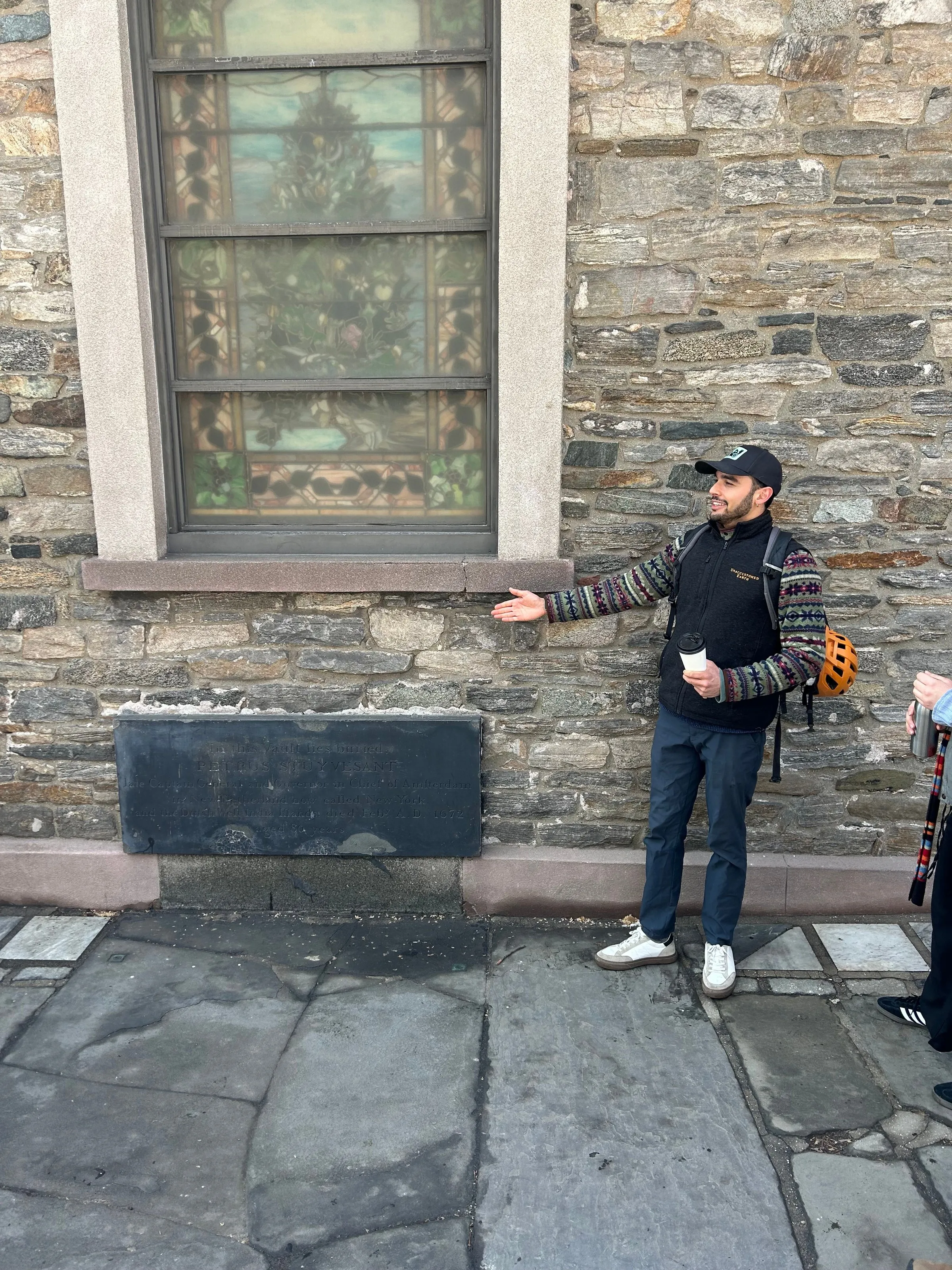 Alex pointing at a stained-glass window in a stone building during a tour