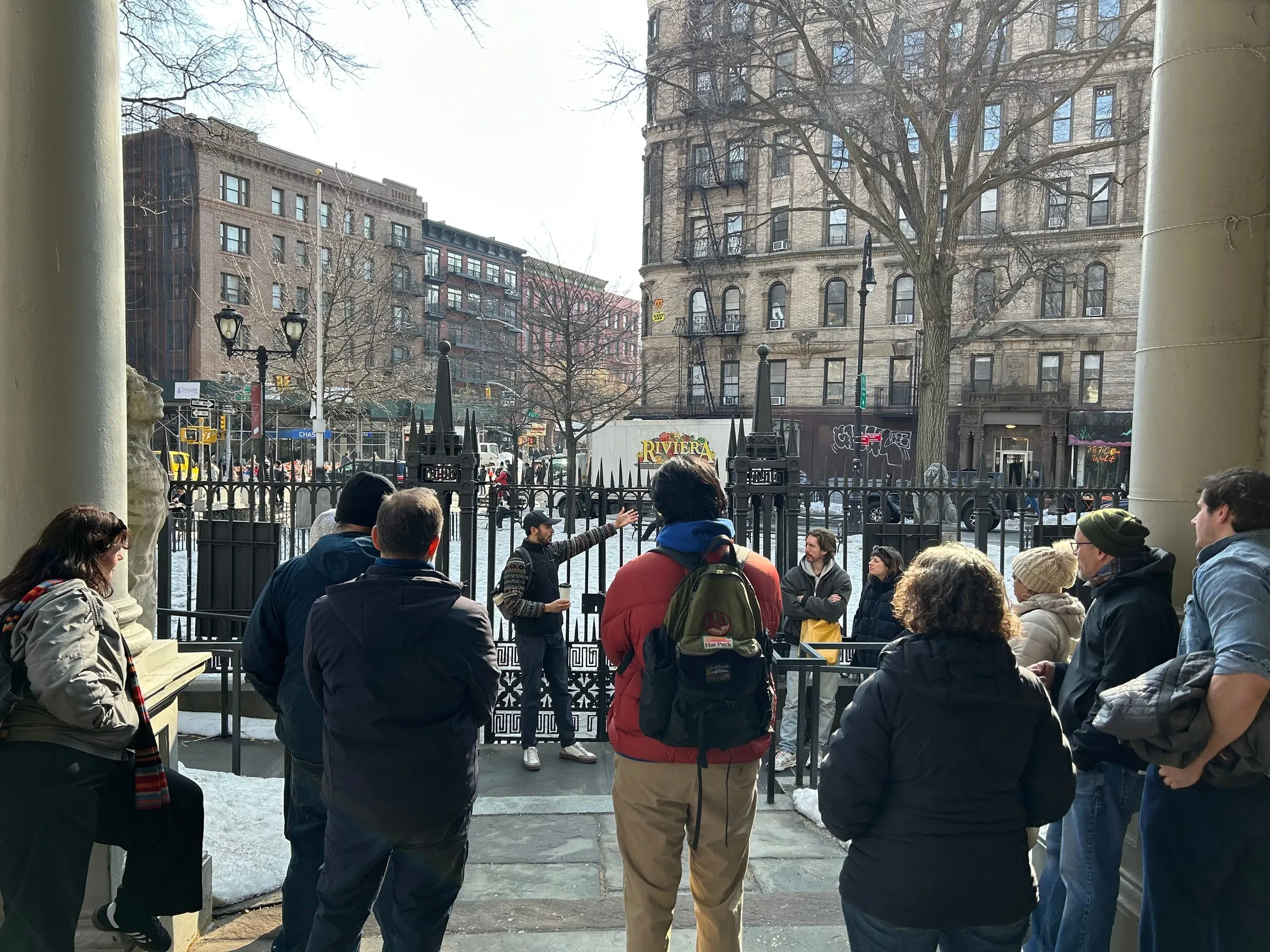 A tour group framed between columns of a portico, looking out at a Manhattan tenement
